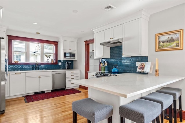 kitchen with visible vents, under cabinet range hood, appliances with stainless steel finishes, a peninsula, and a sink