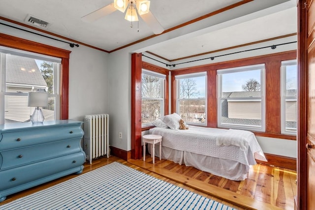 bedroom featuring visible vents, baseboards, radiator heating unit, ornamental molding, and wood-type flooring