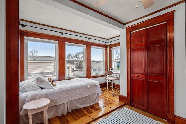 bedroom with baseboards, light wood-style flooring, ceiling fan, ornamental molding, and a closet