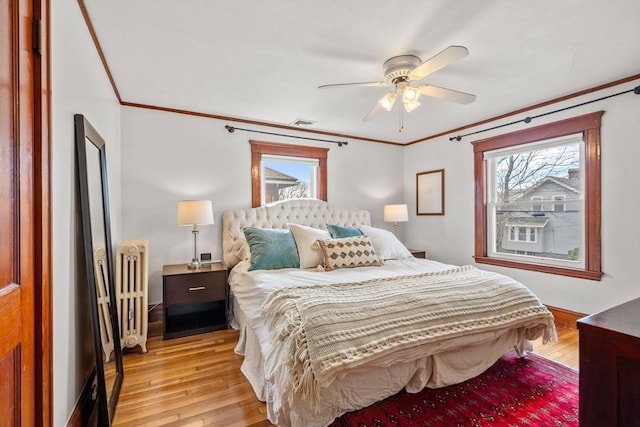 bedroom featuring multiple windows, radiator, and light wood-style floors