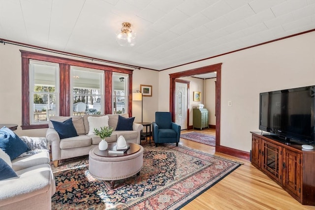 living area with baseboards, light wood-type flooring, and ornamental molding