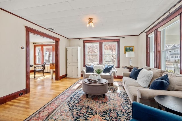 living area featuring baseboards, light wood-style floors, visible vents, and ornamental molding