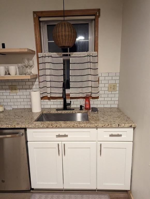 kitchen with white cabinets, a sink, stainless steel dishwasher, and light stone countertops