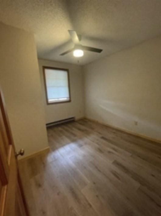 unfurnished bedroom featuring baseboards, ceiling fan, a baseboard heating unit, and wood finished floors