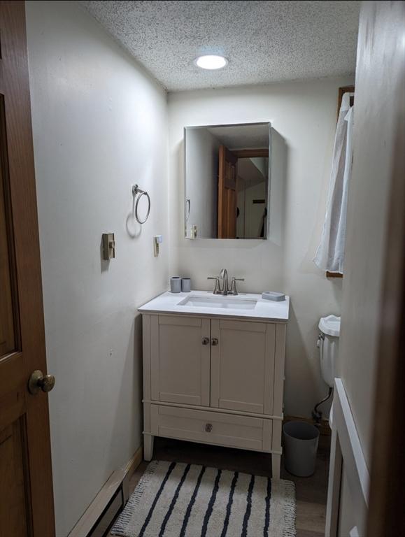 bathroom with a textured ceiling, toilet, wood finished floors, vanity, and baseboards