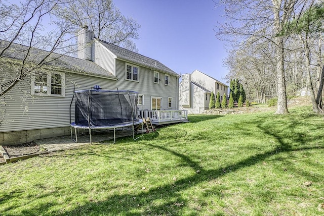 56 Ireta Rd, Shrewsbury, MA 01545 - rear view of property featuring a chimney, a wooden deck, a trampoline, a yard, and roof with shingles