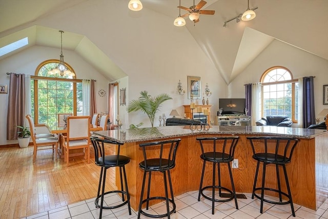 kitchen featuring a kitchen breakfast bar, dark stone counters, lofted ceiling with skylight, ceiling fan, and light tile patterned floors