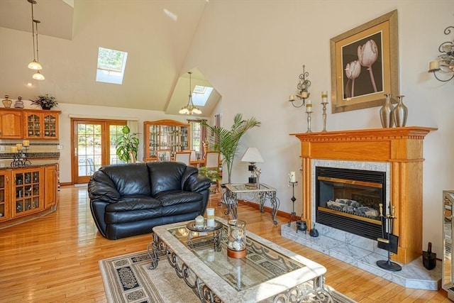 living room with a high end fireplace, light wood-type flooring, a skylight, and high vaulted ceiling