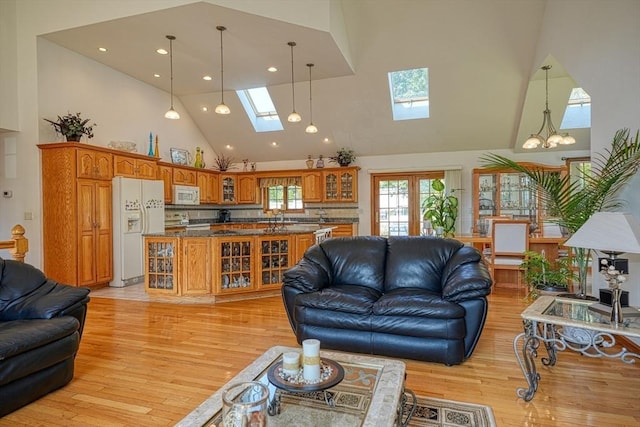 living room with a chandelier, light hardwood / wood-style flooring, high vaulted ceiling, and a skylight