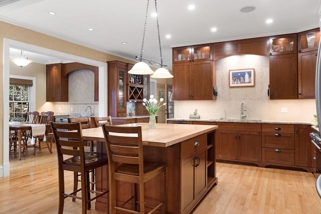 kitchen with light wood finished floors, wooden counters, a center island, and decorative light fixtures