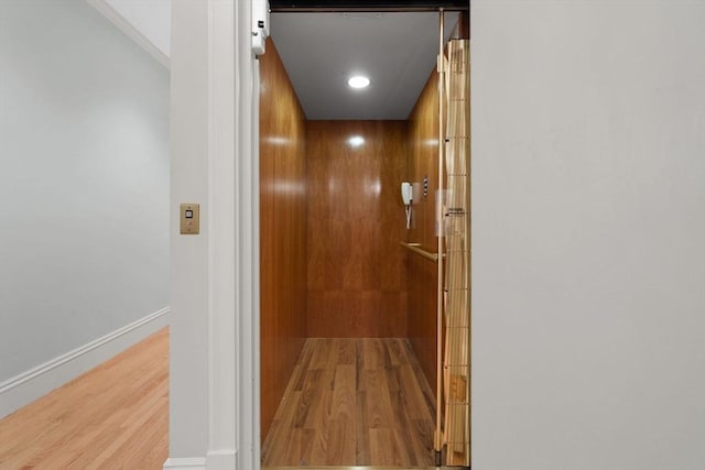 corridor featuring elevator, baseboards, and wood finished floors