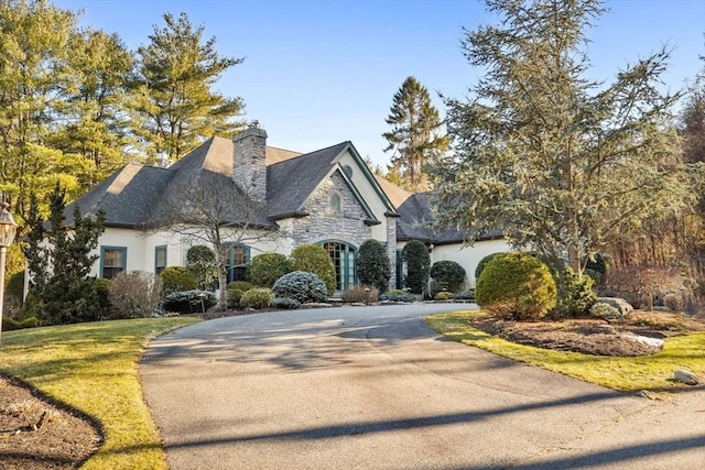 view of front facade with a front lawn, stucco siding, a chimney, stone siding, and driveway