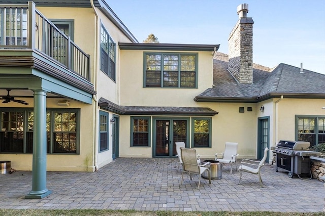 rear view of property with stucco siding, a patio, a fire pit, a shingled roof, and a chimney