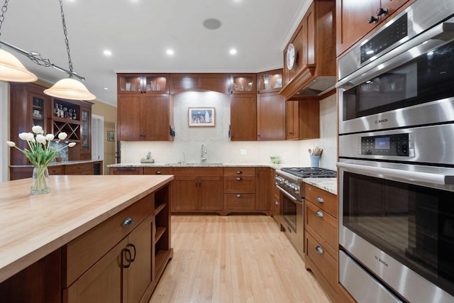 kitchen featuring pendant lighting, butcher block counters, brown cabinets, appliances with stainless steel finishes, and a sink