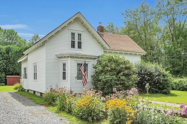 view of front of home with driveway, a shingled roof, and a chimney