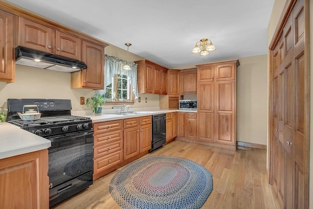 kitchen with under cabinet range hood, light countertops, black appliances, light wood finished floors, and decorative light fixtures