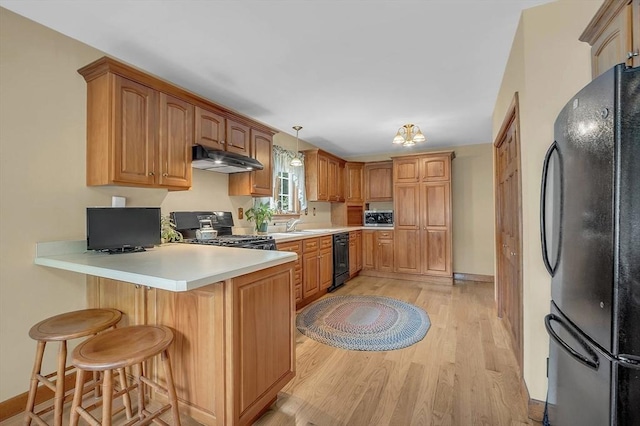 kitchen featuring a breakfast bar area, a peninsula, light wood-type flooring, under cabinet range hood, and black appliances