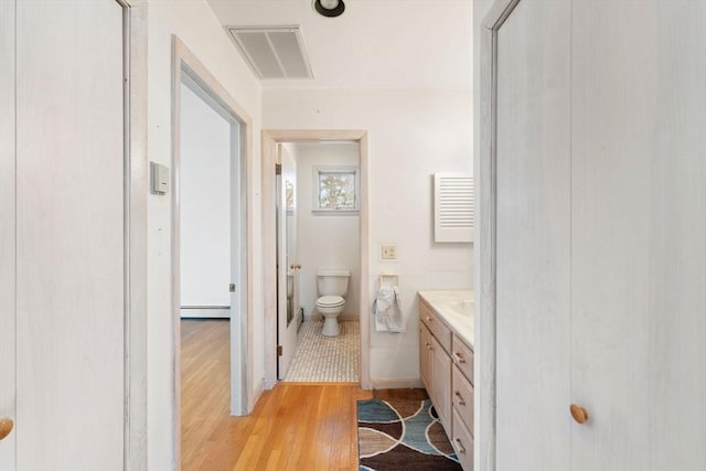 bathroom featuring vanity, wood finished floors, visible vents, a baseboard heating unit, and toilet