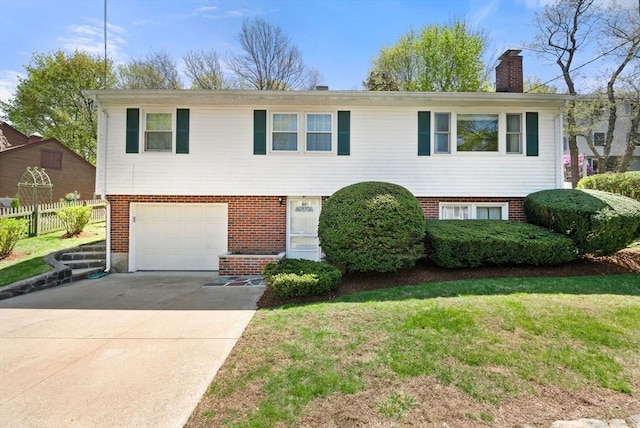 raised ranch featuring driveway, a chimney, a garage, brick siding, and fence