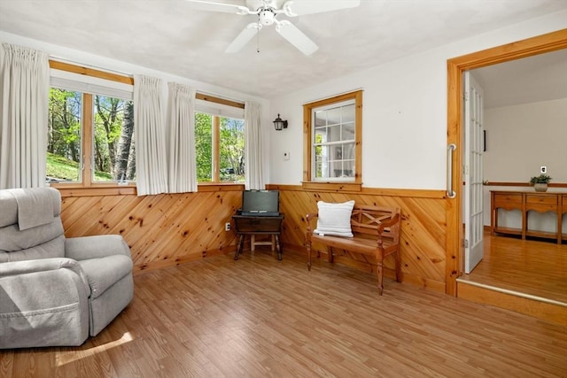 living area with a ceiling fan, wood walls, wainscoting, and wood finished floors