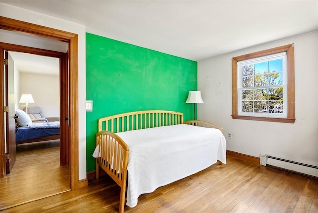 bedroom featuring baseboards, an accent wall, a baseboard heating unit, and wood finished floors