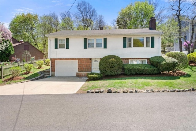 bi-level home featuring a garage, fence, a chimney, brick siding, and driveway
