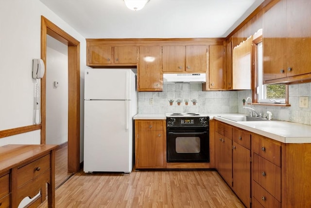 kitchen with black electric range, freestanding refrigerator, under cabinet range hood, and brown cabinets