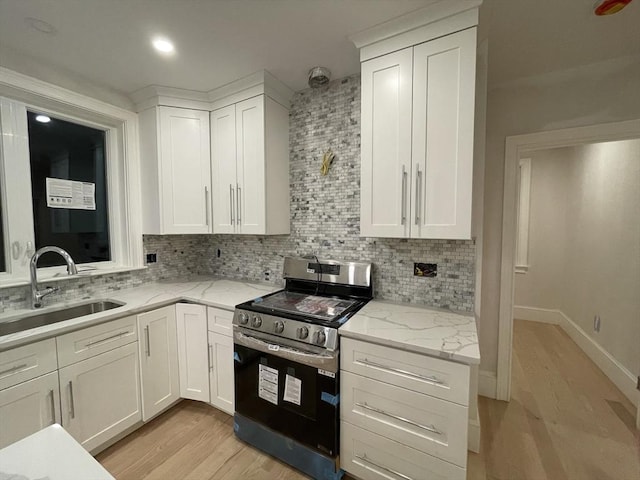 kitchen with white cabinetry, stainless steel range, decorative backsplash, and a sink