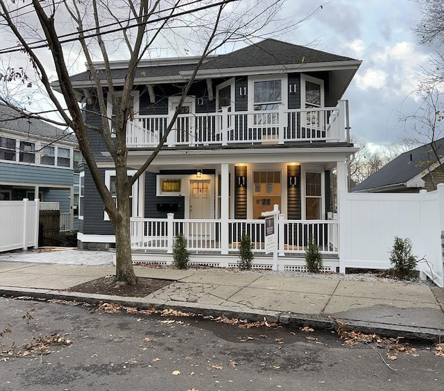 view of front of house featuring covered porch, fence, and a balcony