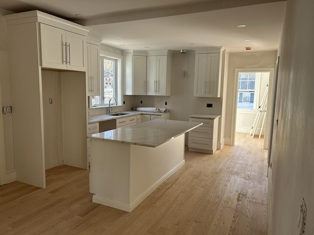 kitchen featuring a kitchen island, a sink, light wood-style flooring, and light stone counters