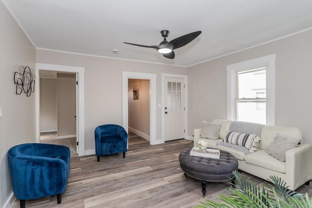 living area featuring ceiling fan, ornamental molding, light wood-style flooring, and baseboards