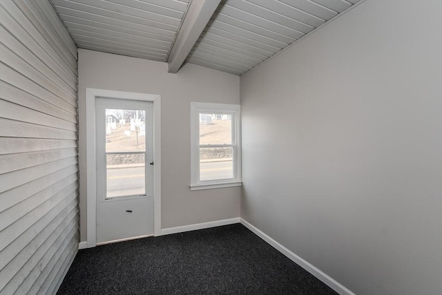 interior space featuring dark colored carpet, beam ceiling, and baseboards