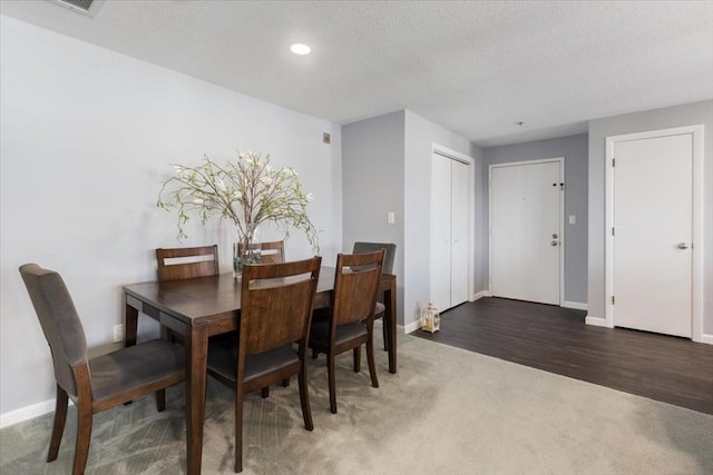 carpeted dining area featuring a textured ceiling, baseboards, and wood finished floors