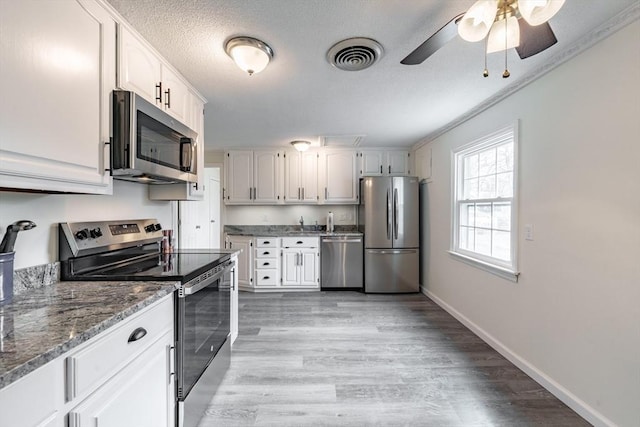 kitchen featuring white cabinets, appliances with stainless steel finishes, dark stone counters, ceiling fan, and light hardwood / wood-style flooring