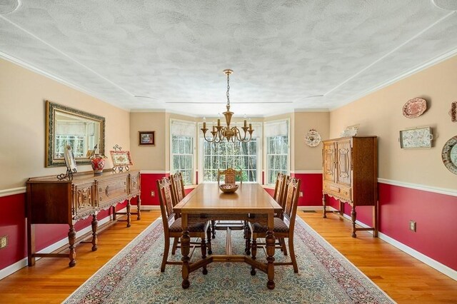 dining area with a chandelier, wood finished floors, baseboards, crown molding, and a textured ceiling