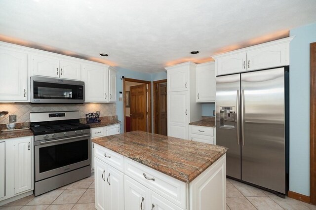 kitchen featuring appliances with stainless steel finishes, light tile patterned flooring, dark stone counters, white cabinetry, and recessed lighting