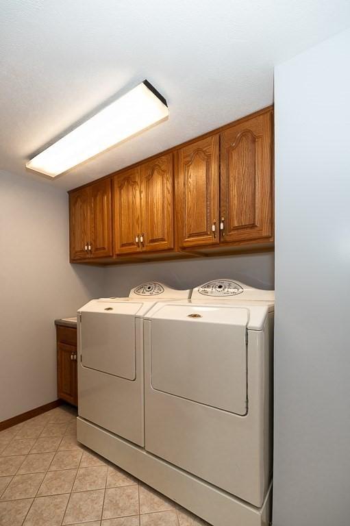 laundry area with cabinet space, washer and dryer, light tile patterned floors, and baseboards