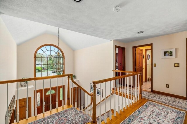 hallway featuring wood finished floors, vaulted ceiling, an upstairs landing, baseboards, and a textured ceiling
