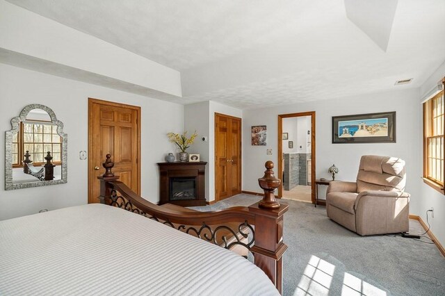 carpeted bedroom with baseboards, a glass covered fireplace, and connected bathroom