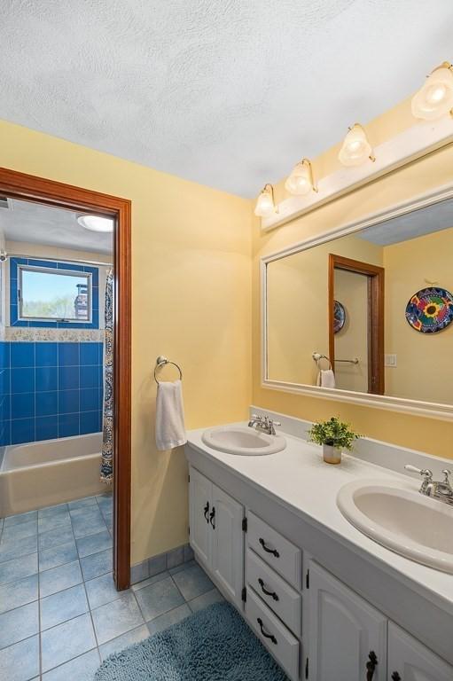 full bath featuring tile patterned flooring, double vanity, shower / bath combination with curtain, and a textured ceiling