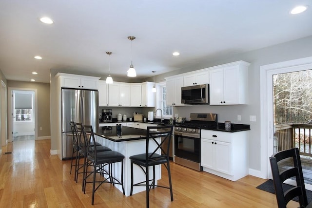 kitchen with sink, white cabinetry, stainless steel appliances, a kitchen breakfast bar, and decorative light fixtures