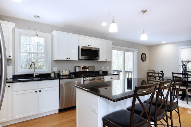 kitchen featuring sink, appliances with stainless steel finishes, white cabinets, a kitchen island, and decorative light fixtures