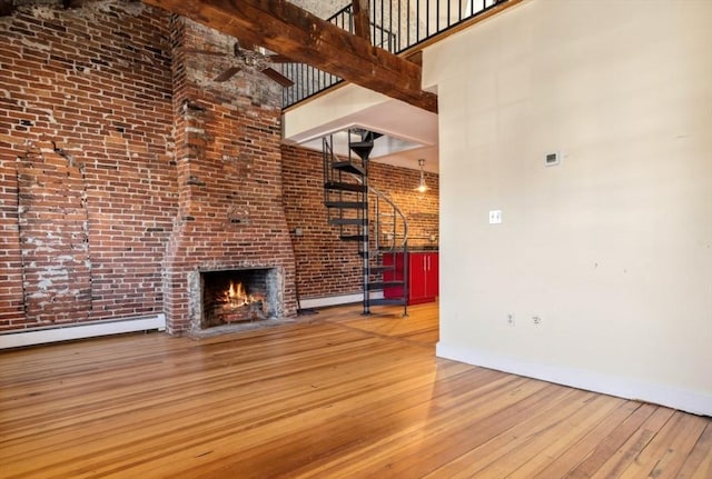 unfurnished living room with wood-type flooring, a baseboard heating unit, a high ceiling, and a fireplace