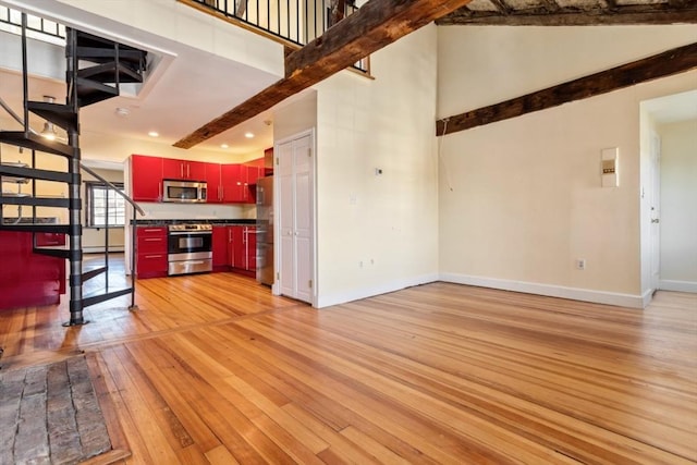 unfurnished living room with light wood-type flooring, baseboard heating, beamed ceiling, and a high ceiling