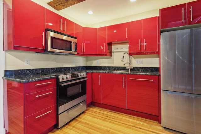 kitchen featuring appliances with stainless steel finishes, sink, light wood-type flooring, and dark stone countertops