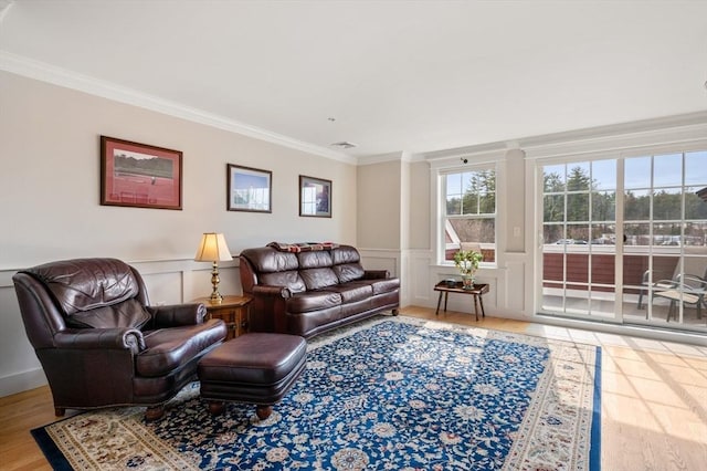 living area featuring visible vents, a decorative wall, ornamental molding, wainscoting, and wood finished floors