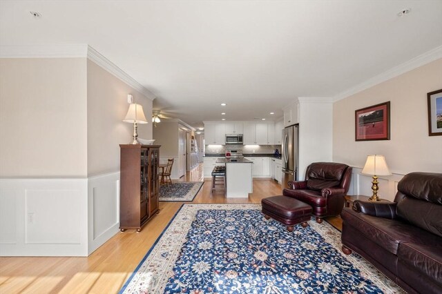 living area featuring recessed lighting, a ceiling fan, ornamental molding, wainscoting, and light wood finished floors