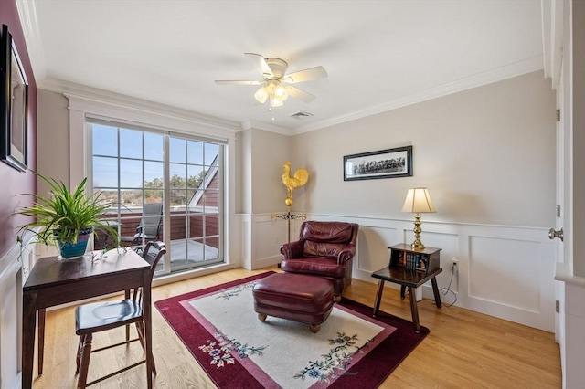 living area featuring ornamental molding, light wood finished floors, wainscoting, and visible vents