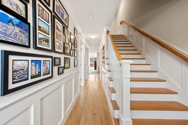 stairs with ornamental molding, a decorative wall, and wood finished floors