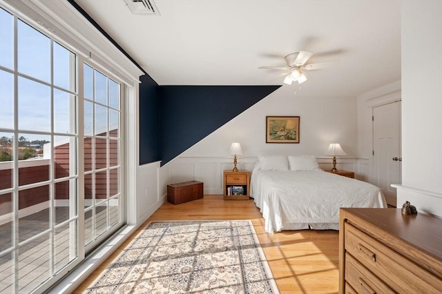 bedroom with wainscoting, visible vents, a decorative wall, and wood finished floors